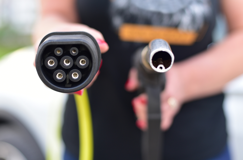 Electric vehicle charging cable versus gas pump nozzle showing powertrain comparison options